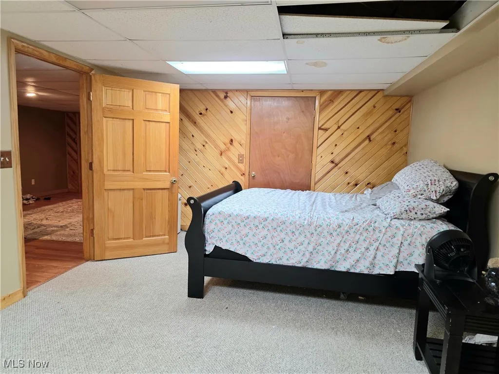 Bedroom featuring carpet, a paneled ceiling, and wooden walls