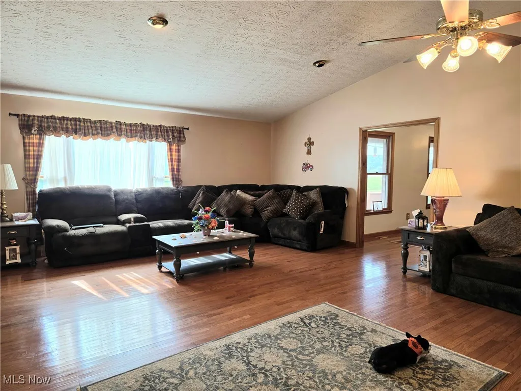 Living area featuring wood finished floors, a textured ceiling, ceiling fan, and lofted ceiling