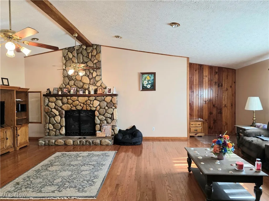 Living room with ceiling fan, a stone fireplace, a textured ceiling, and wood finished floors