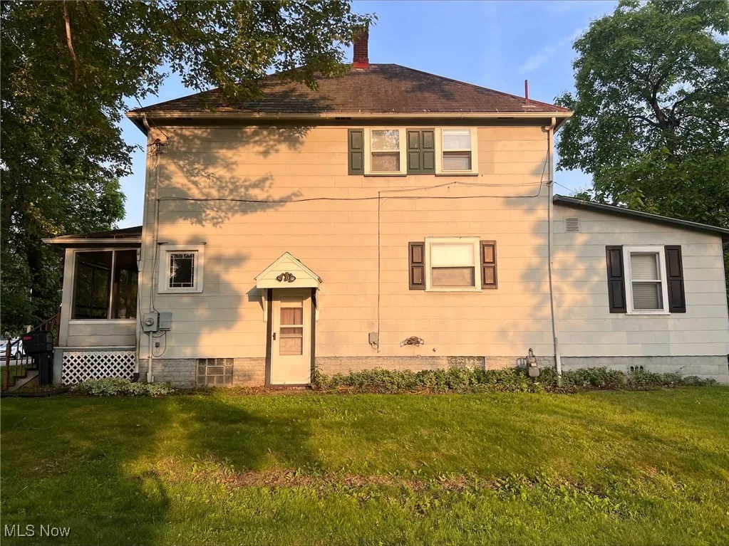 Back of house featuring a lawn, a sunroom, and a chimney