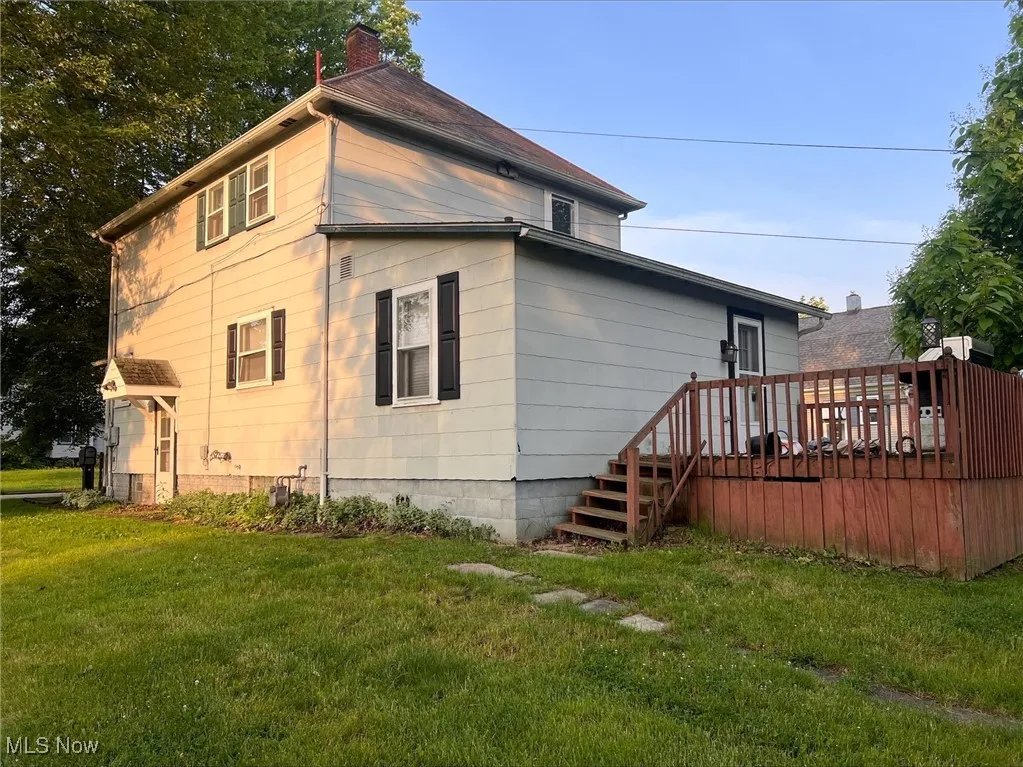 View of property exterior featuring a chimney, a yard, and a deck