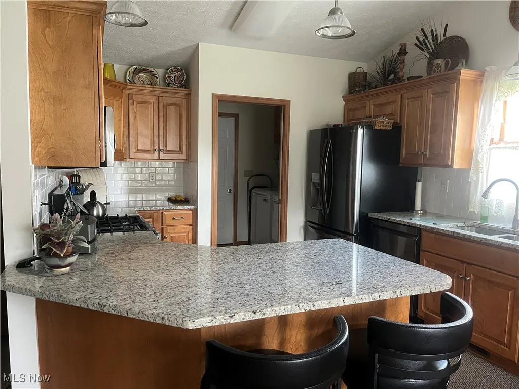 Kitchen featuring a peninsula, backsplash, brown cabinets, fridge with ice dispenser, and a textured ceiling