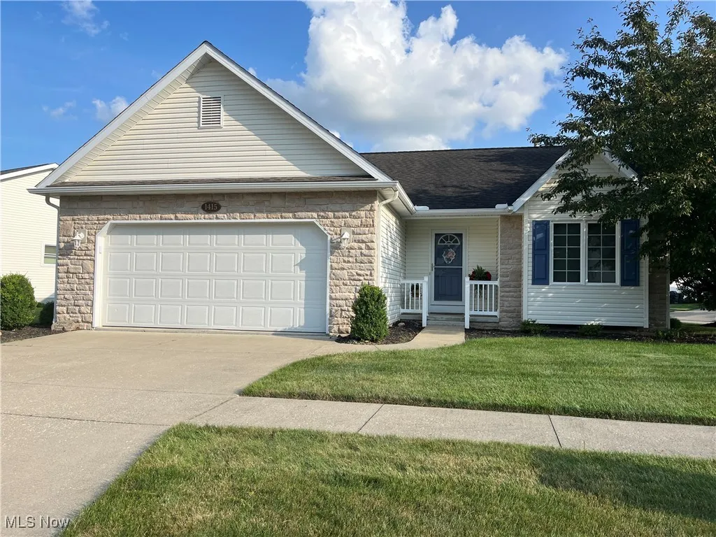 Single story home featuring concrete driveway, an attached garage, stone siding, a front lawn, and covered porch