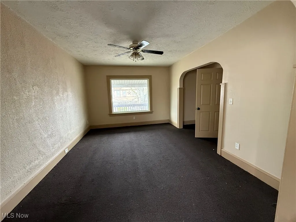 Spare room with ceiling fan, arched walkways, a textured ceiling, a textured wall, and dark carpet