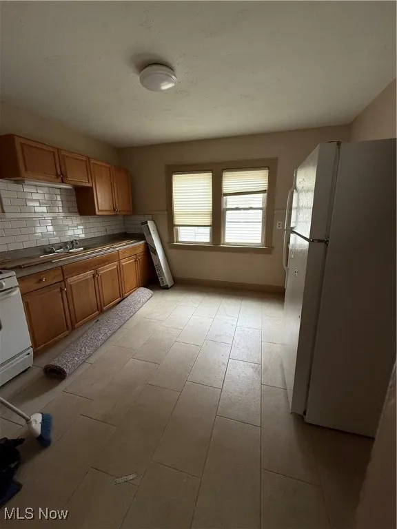 Kitchen with refrigerator, range, tasteful backsplash, brown cabinetry, and dark countertops