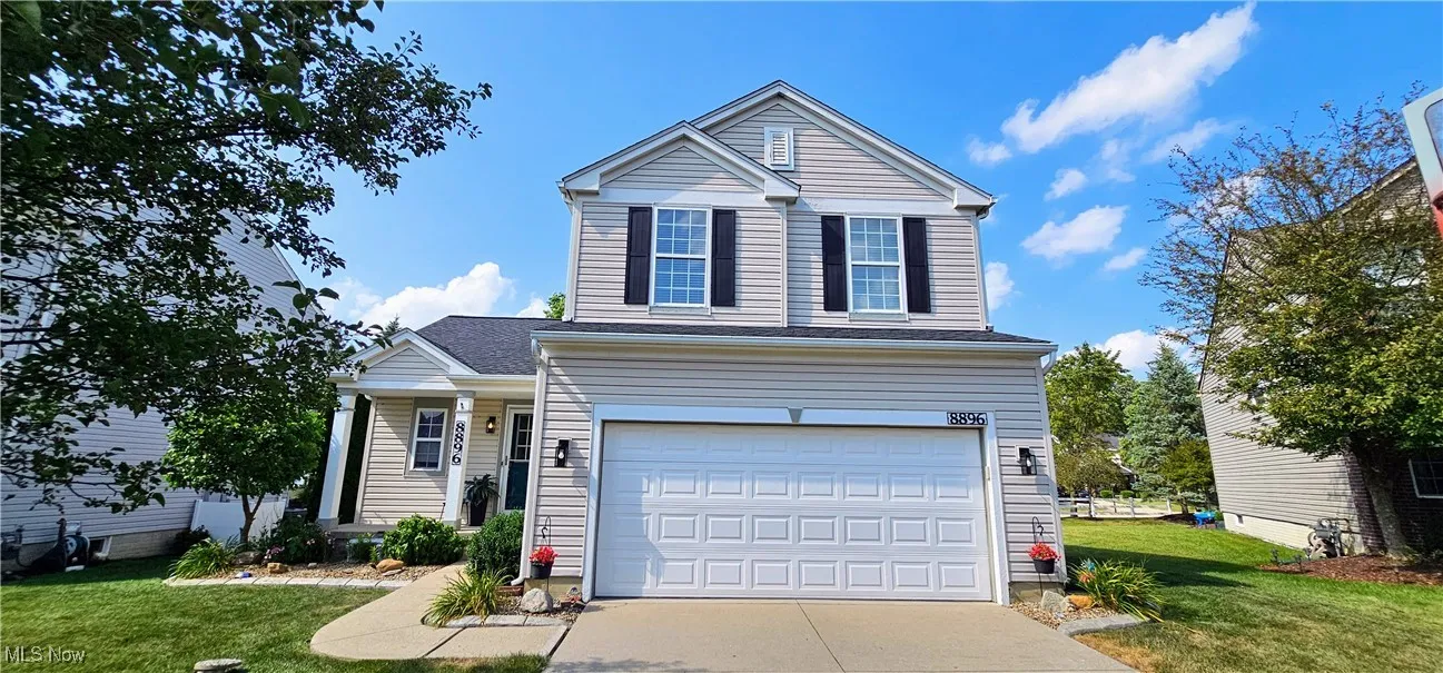 Traditional-style house with driveway, a front yard, an attached garage, and a shingled roof