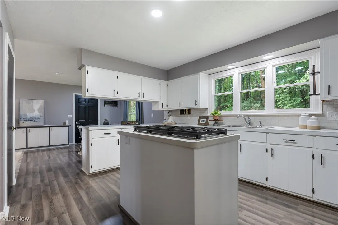 Kitchen featuring dark wood-style flooring, decorative backsplash, stainless steel gas cooktop, white cabinetry, and a kitchen island