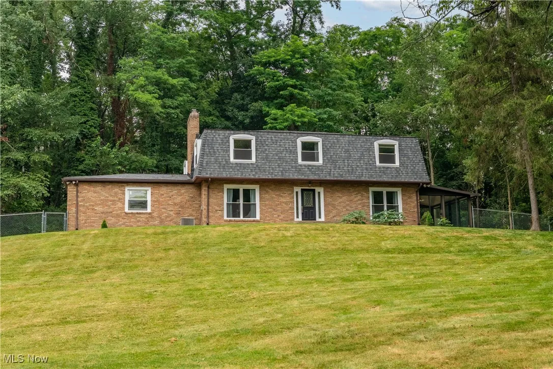 View of property with brick siding, mansard roof, a chimney, and a shingled roof