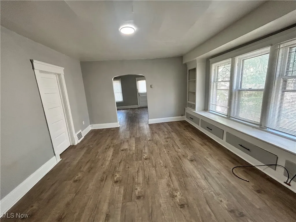 Empty room with arched walkways, dark wood-style flooring, and built in shelves