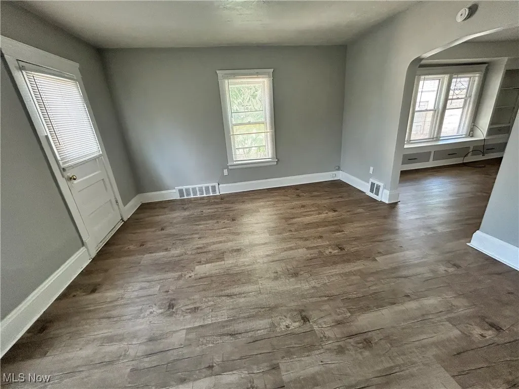 Spare room featuring healthy amount of natural light, arched walkways, and dark wood-type flooring