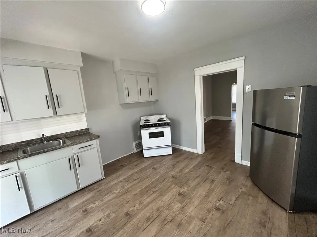 Kitchen featuring freestanding refrigerator, white electric stove, white cabinets, and wood finished floors