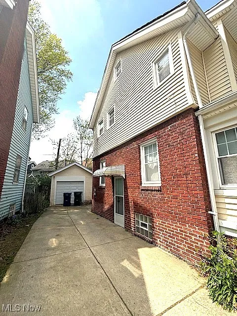 View of side of home featuring a detached garage, brick siding, an outbuilding, and concrete driveway