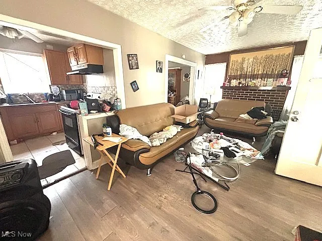 Living room with ceiling fan, light wood-style flooring, and a textured ceiling