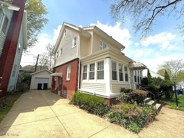 View of side of home with a detached garage, an outbuilding, brick siding, and concrete driveway