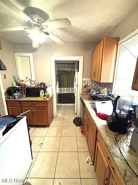 Kitchen with a textured ceiling, light tile patterned floors, range, ceiling fan, and brown cabinetry