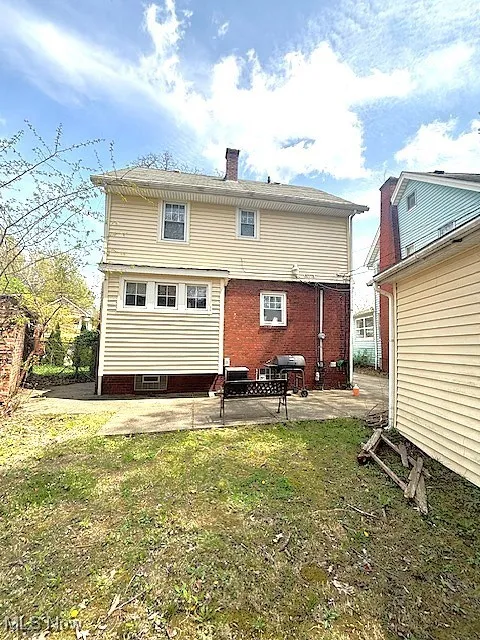 Rear view of house with a patio, a chimney, and a lawn
