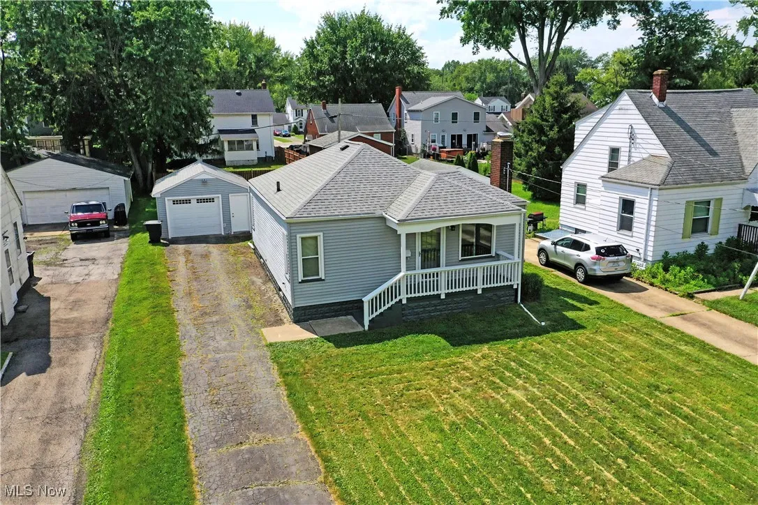 View of front of home featuring a porch, a detached garage, a front lawn, and driveway