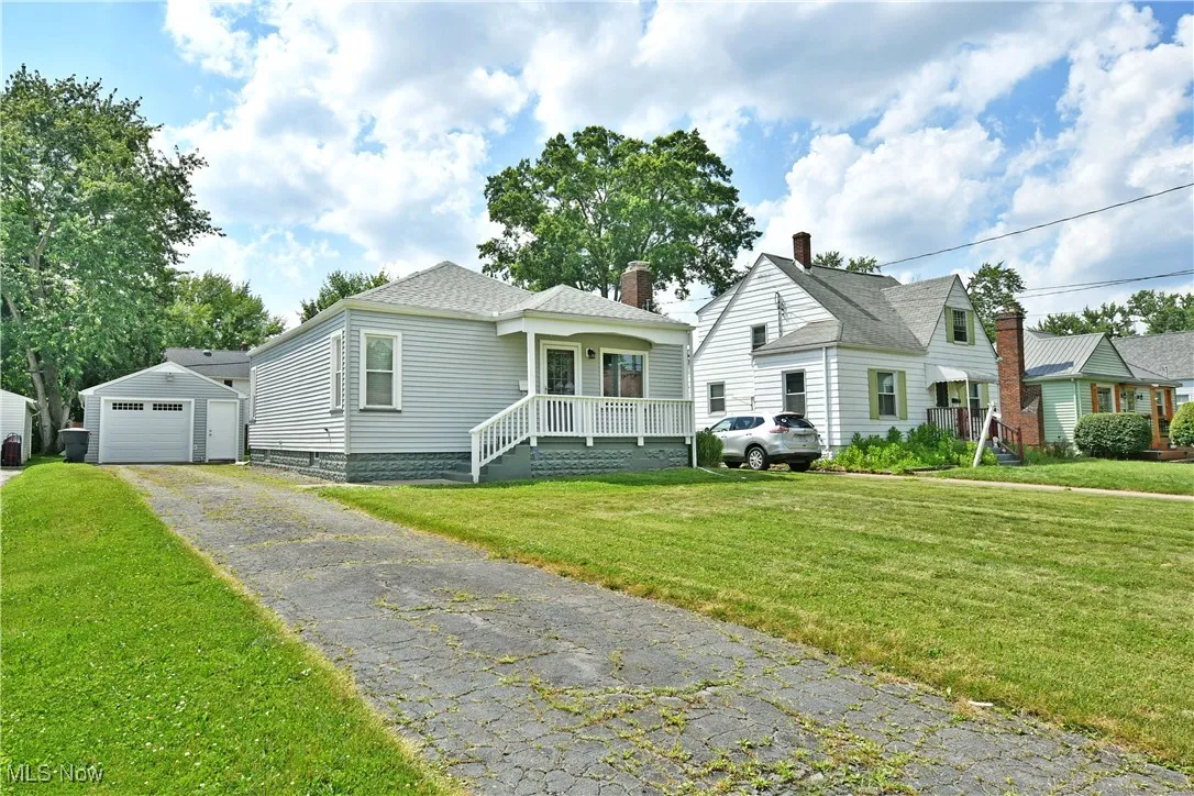Bungalow-style house featuring a garage, an outdoor structure, asphalt driveway, a front lawn, and a chimney