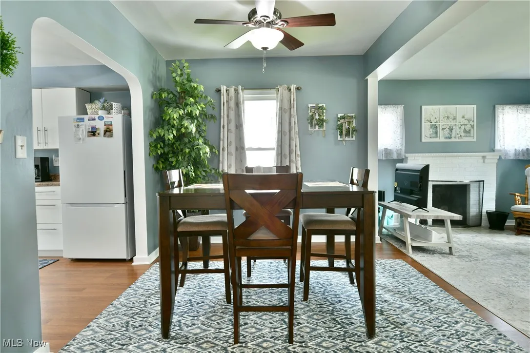 Dining room with ceiling fan, wood finished floors, arched walkways, and a brick fireplace