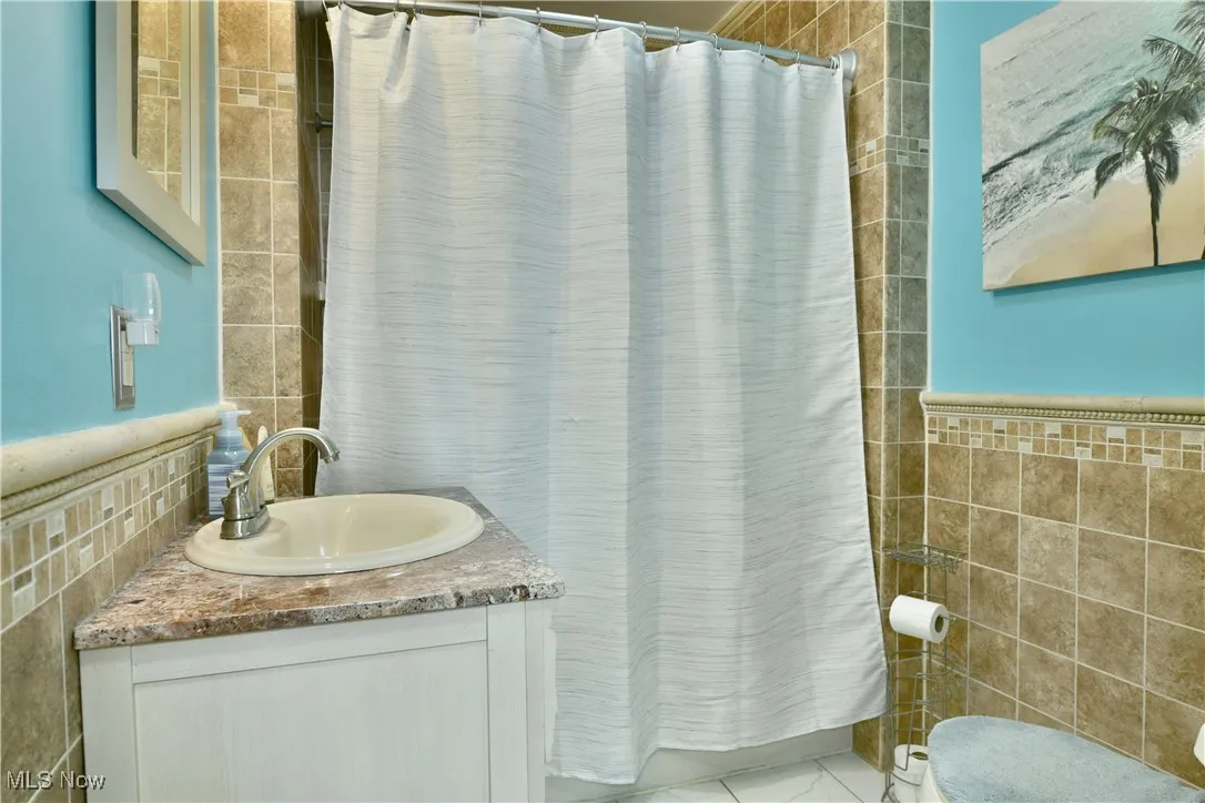 Full bath featuring tile walls, vanity, and a shower with shower curtain