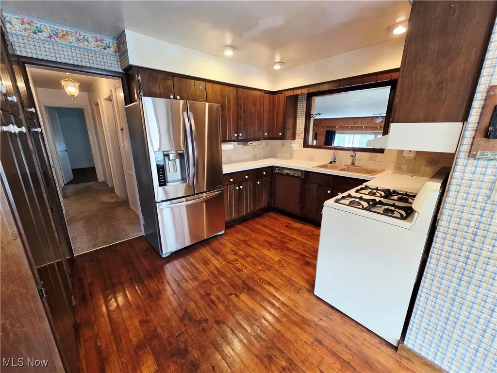 Kitchen with stainless steel refrigerator with ice dispenser, gas range gas stove, dark brown cabinets, and dark wood finished floors