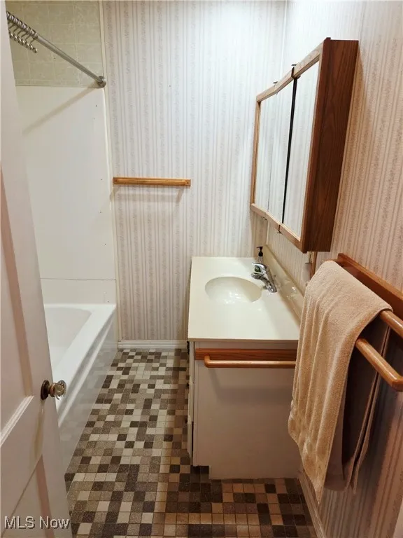 Bathroom with wallpapered walls, vanity, and bathtub / shower combination