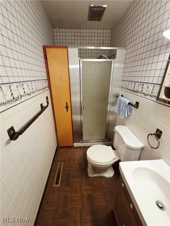 Bathroom with wallpapered walls, tile walls, vanity, a stall shower, and wainscoting