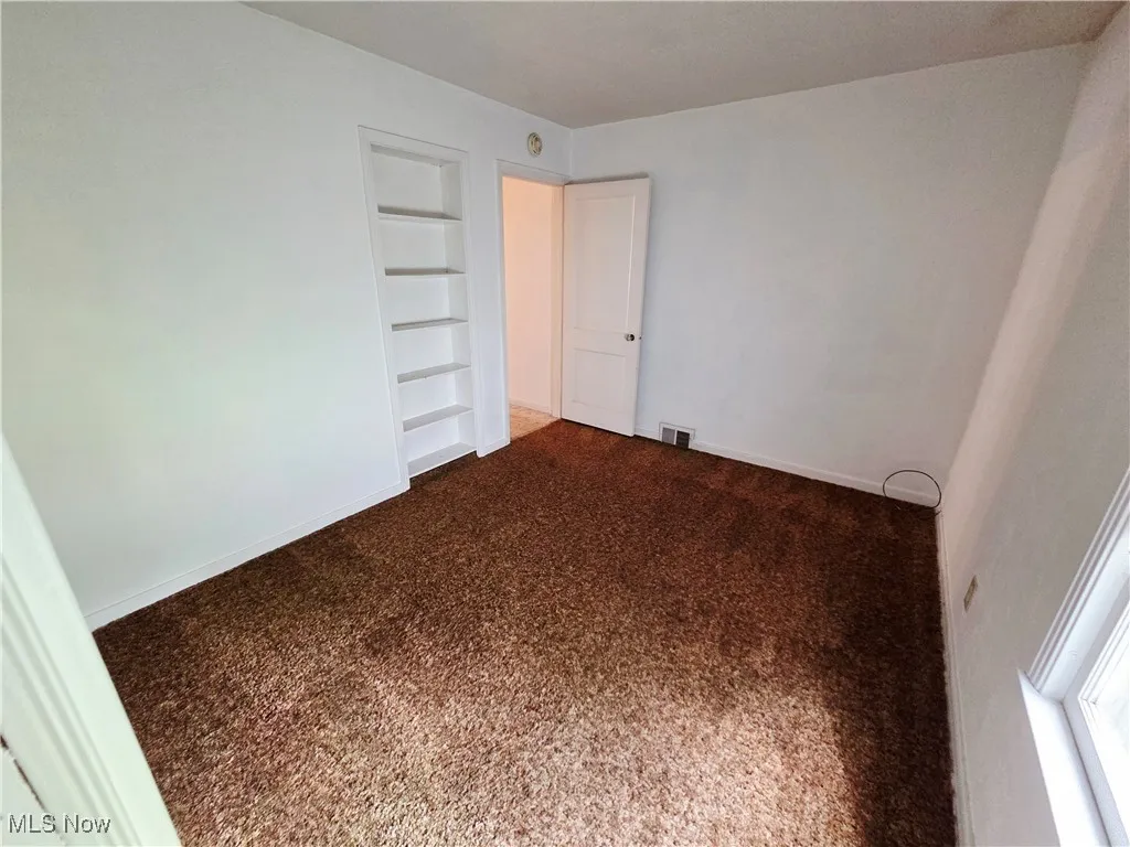 Carpeted empty room with built in features and baseboards