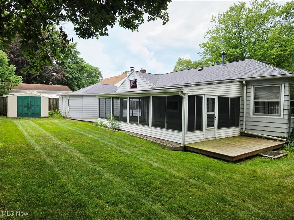 Rear view of property featuring a sunroom, a storage unit, a wooden deck, and roof with shingles