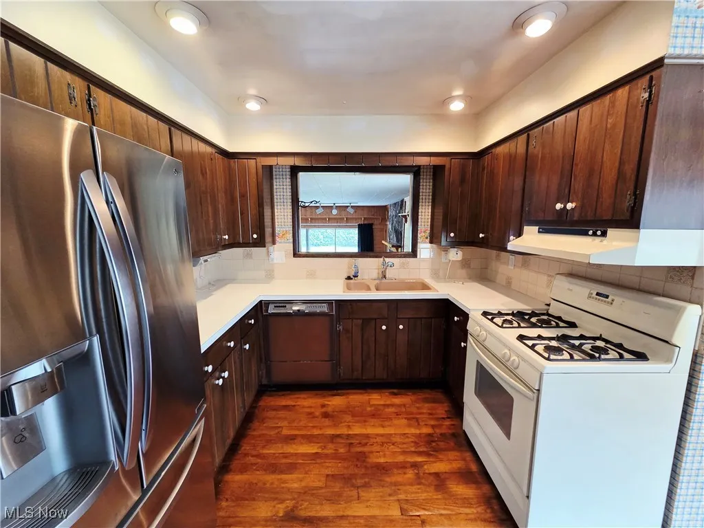 Kitchen with freestanding refrigerator, white range with gas stovetop, dishwasher, light countertops, and dark wood finished floors