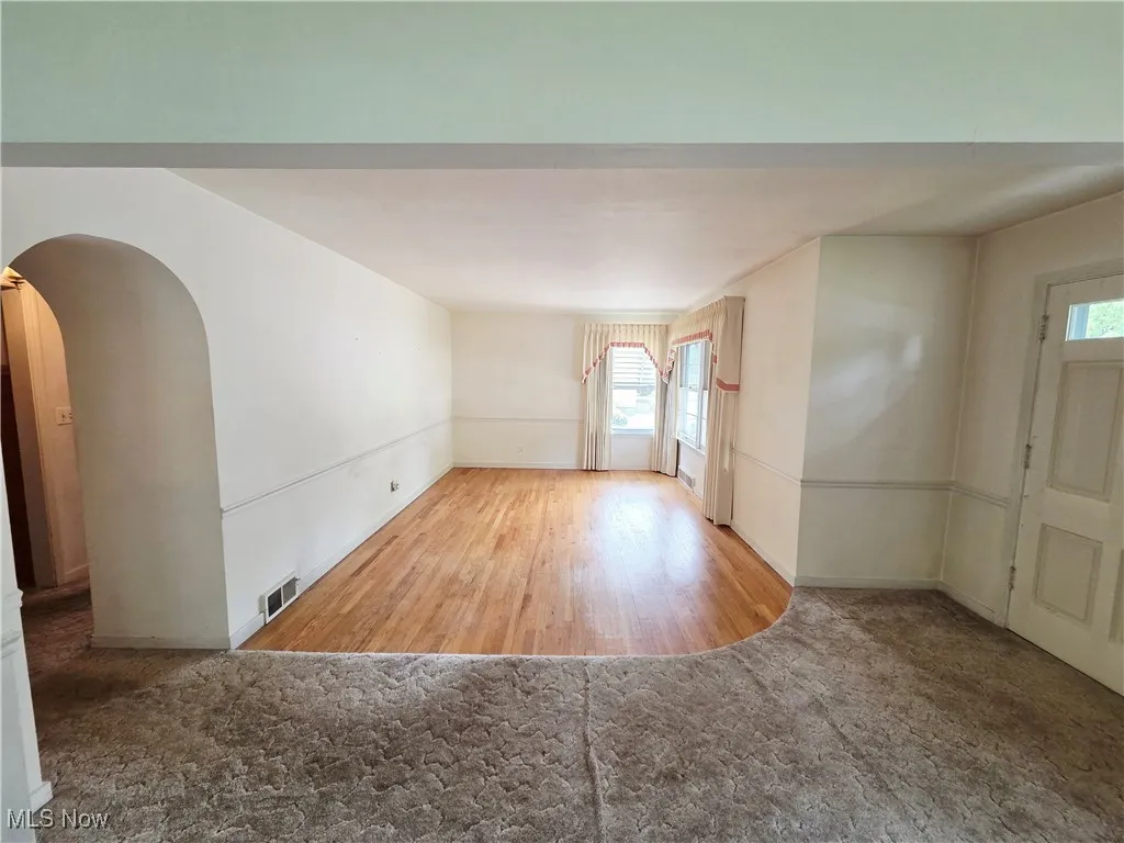 Spare room with arched walkways, healthy amount of natural light, carpet floors, and wood finished floors