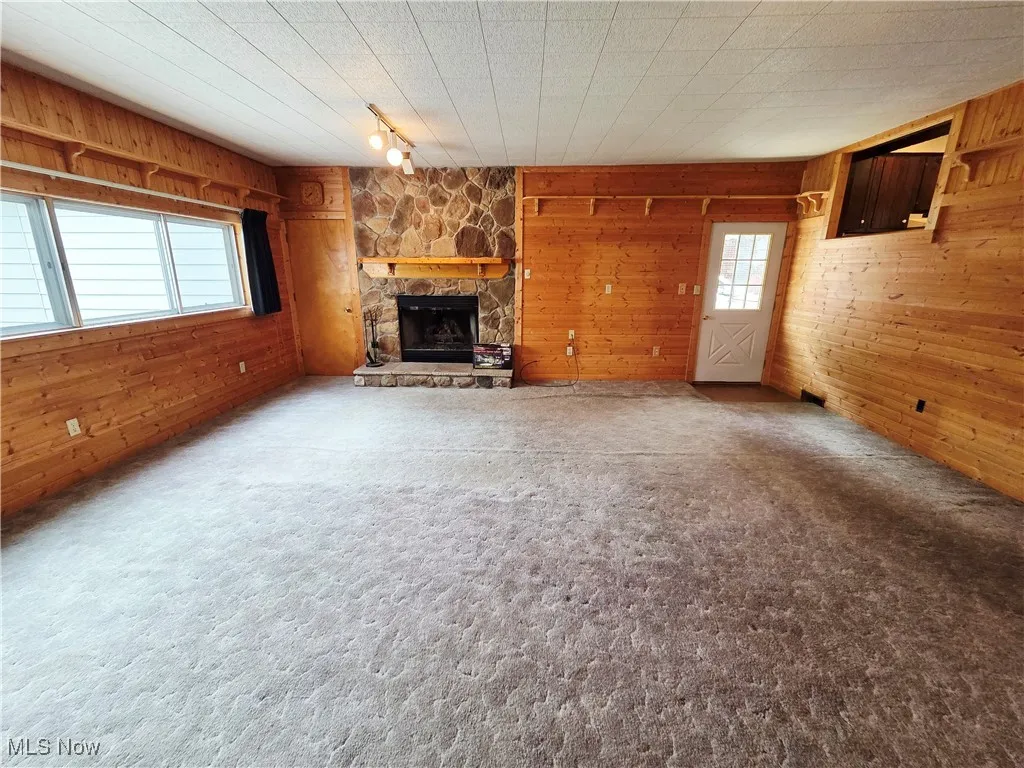 Unfurnished living room with wooden walls, rail lighting, a fireplace, and carpet floors