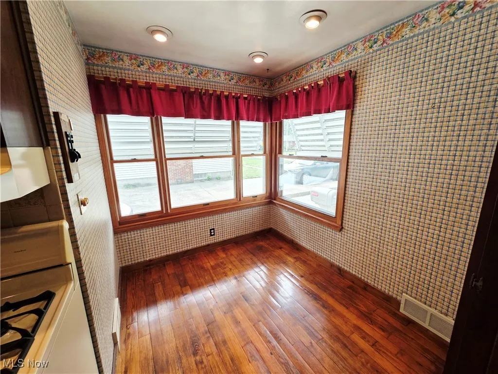Unfurnished dining area with wood-type flooring and wallpapered walls