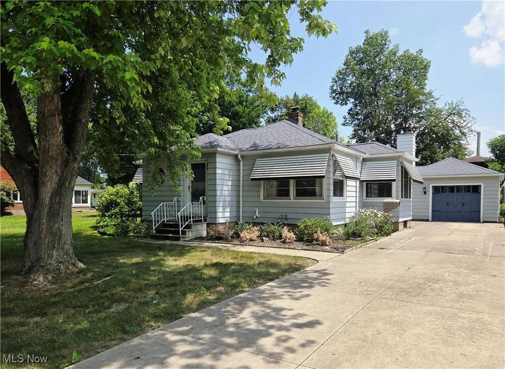 View of front facade featuring a garage, a front lawn, a chimney, driveway, and a shingled roof