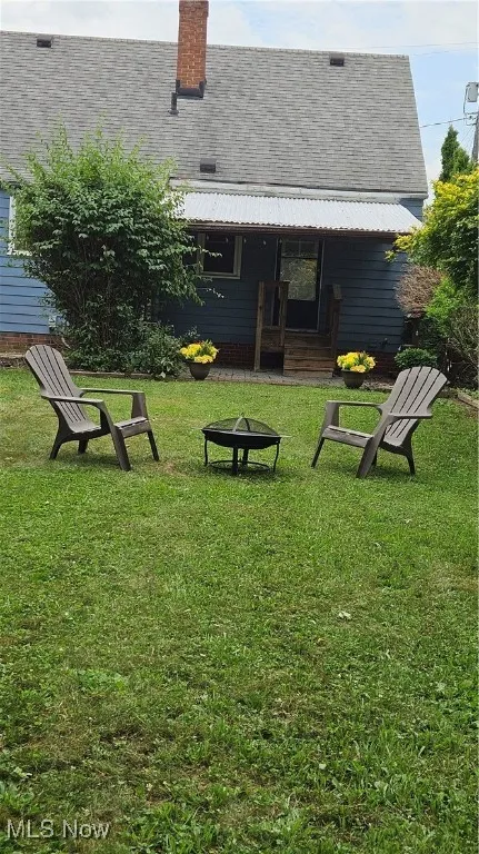 Rear view of house featuring a fire pit, a lawn, a shingled roof, and a chimney