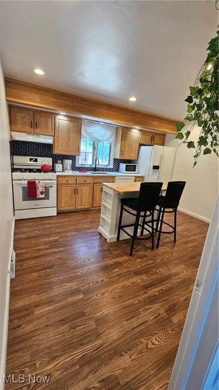 Kitchen with stove, range hood, dark wood finished floors, light countertops, and a kitchen bar