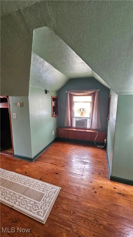 Bonus room with a textured ceiling, cooling unit, hardwood / wood-style flooring, and vaulted ceiling