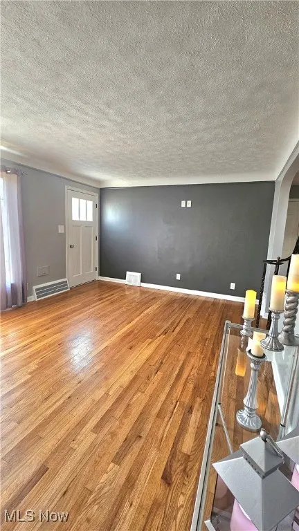 Unfurnished living room featuring a textured ceiling, wood-type flooring, and arched walkways