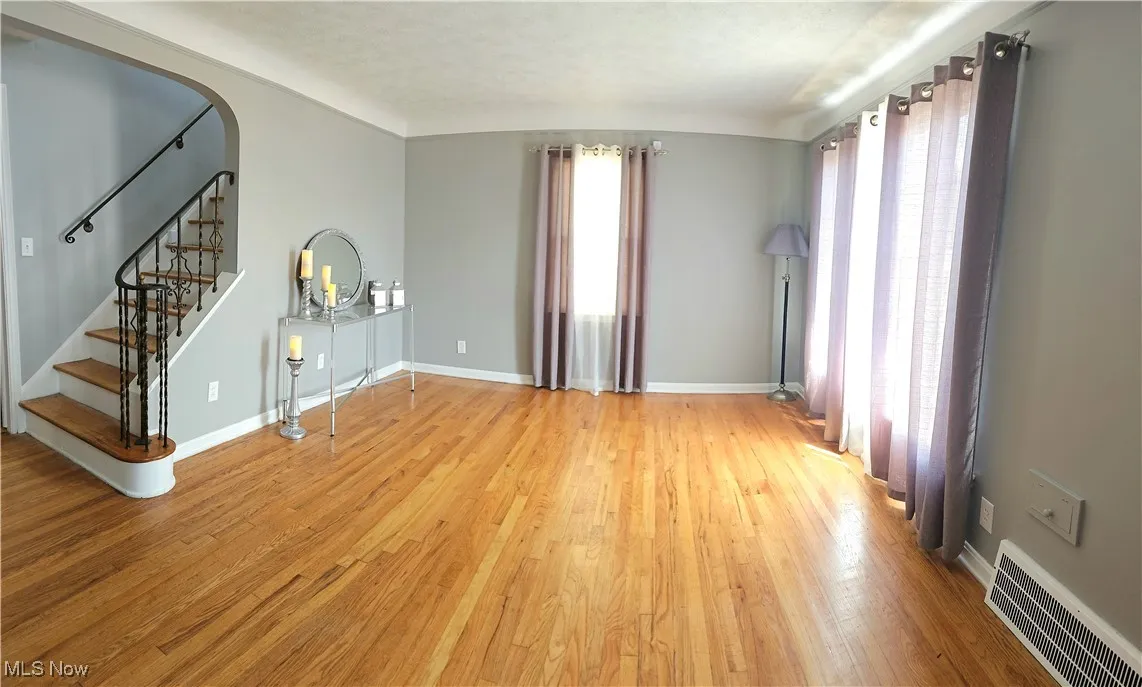 Unfurnished living room with light wood-style flooring, arched walkways, and stairway