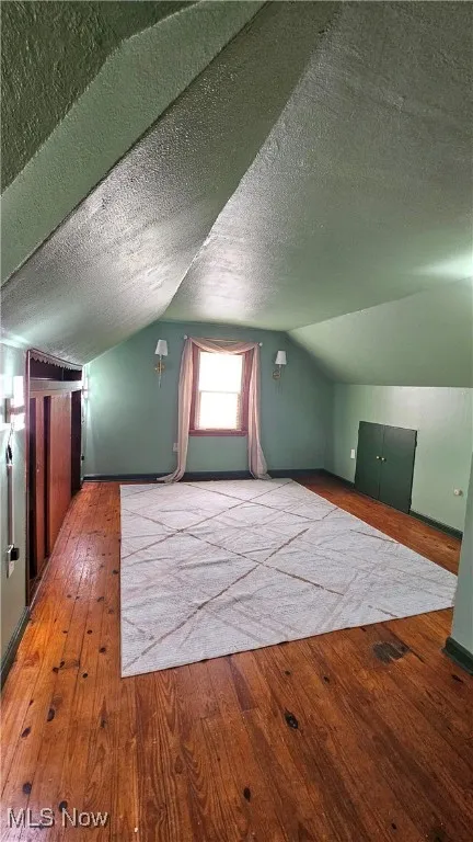 Additional living space featuring hardwood / wood-style floors, lofted ceiling, and a textured ceiling