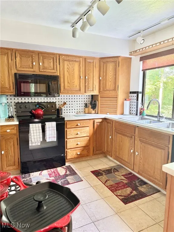 Kitchen featuring black appliances, rail lighting, light countertops, and backsplash