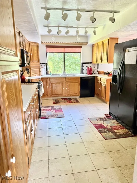 Kitchen featuring black appliances, light countertops, light tile patterned flooring, and rail lighting