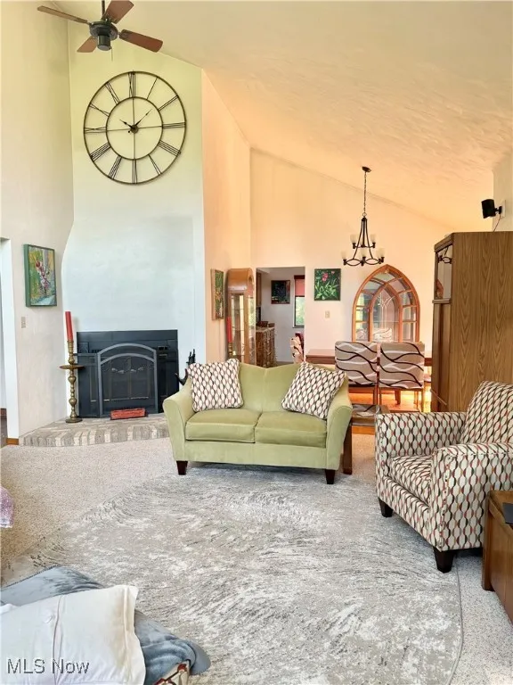 Living room featuring a chandelier, ceiling fan, a fireplace, and high vaulted ceiling