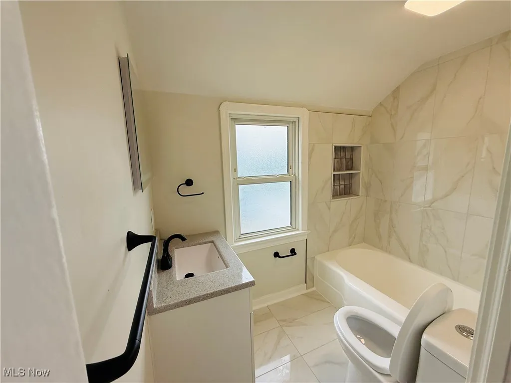 Full bathroom featuring lofted ceiling, vanity, and marble finish flooring