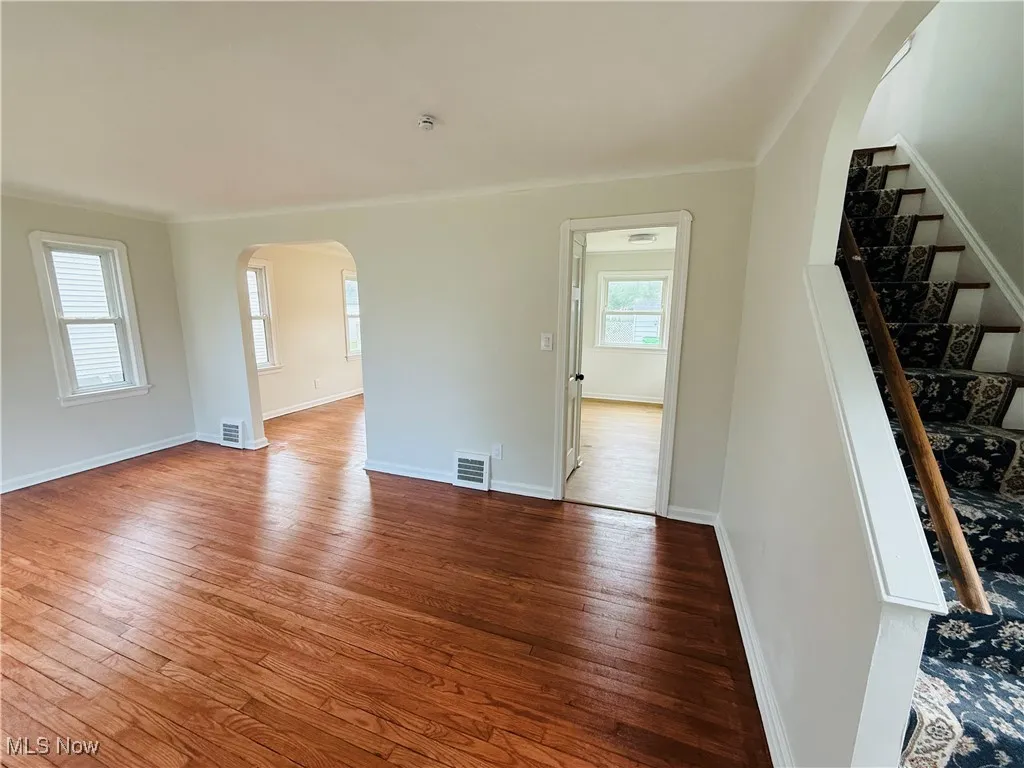 Unfurnished living room with hardwood / wood-style flooring, arched walkways, and stairs