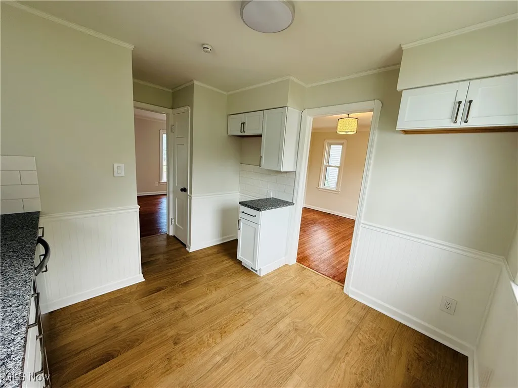 Kitchen with wainscoting, light wood-type flooring, white cabinetry, dark stone counters, and ornamental molding