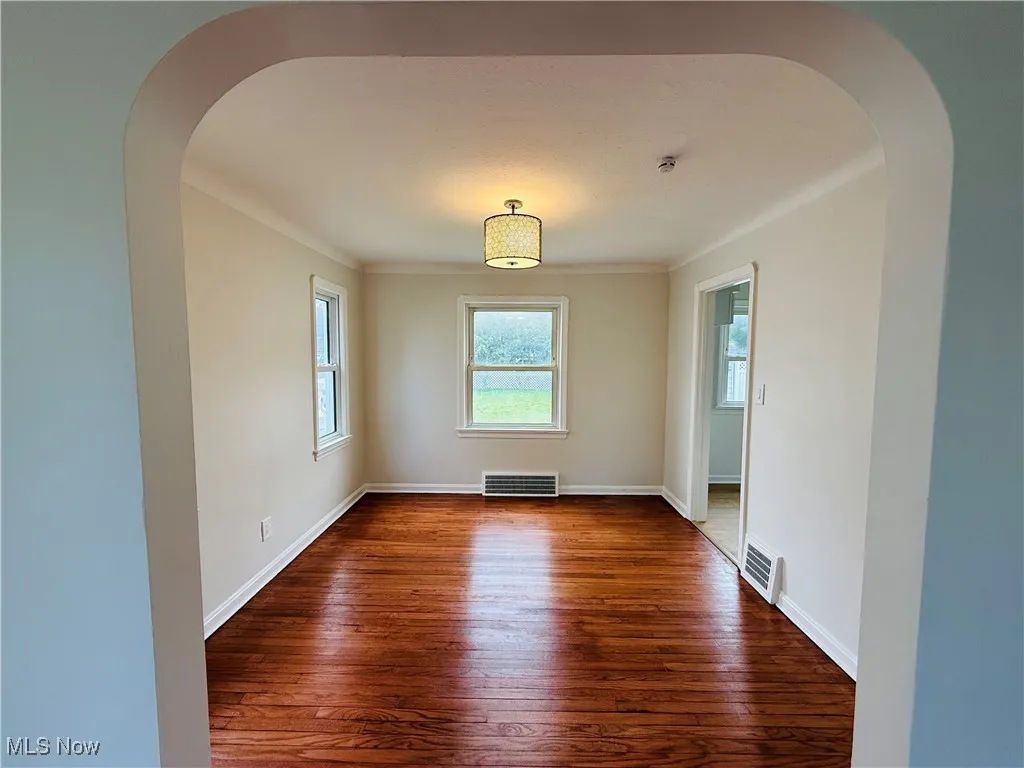 Spare room with dark wood-type flooring, arched walkways, and ornamental molding