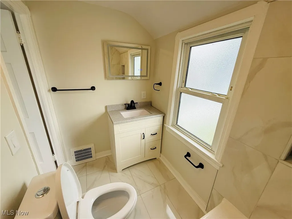 Bathroom featuring vanity, marble look tile flooring, and lofted ceiling