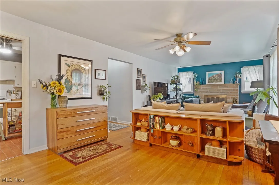 Living room with ceiling fan, light wood flooring, and a fireplace