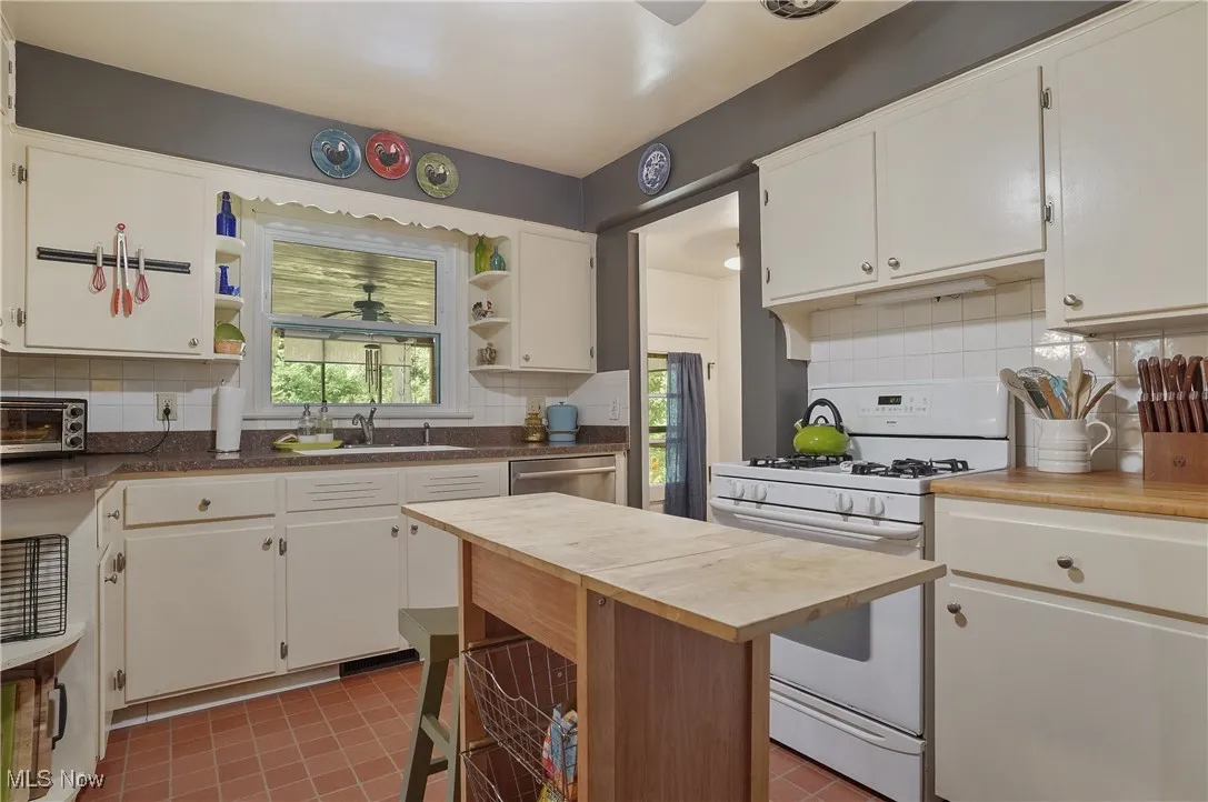 Kitchen with white gas stove, open shelves, butcher block countertops, decorative backsplash, and dishwasher